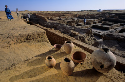 image of several old, damaged earthenware vases sitting on a ledge overlooking an area of dug out excavation